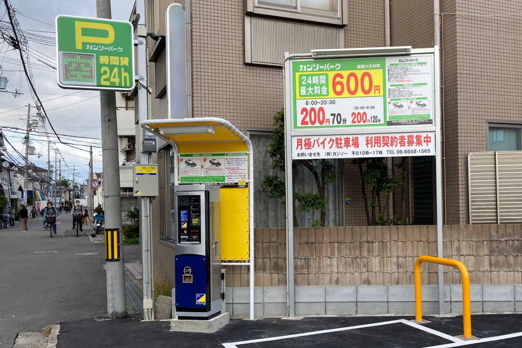 数台分の駐車スペース、自動精算機、24時間営業の看板などが設置された、住宅地にある小規模な有料駐車場