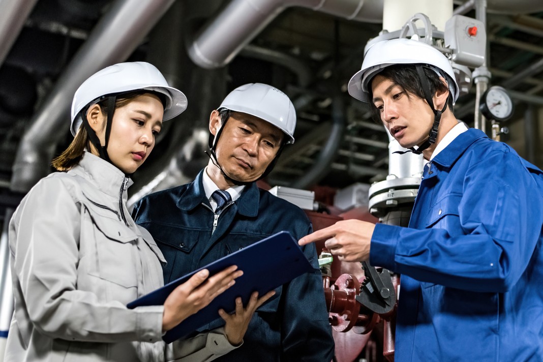 ヘルメット姿のスタッフ3名が現場にて資料を見ながら綿密な打ち合わせを行っている様子